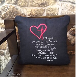 May include: Black throw pillow with white text and a pink heart with a cross inside. The text reads "For God so loved the world that he gave his one and only Son, that whoever believes in him shall not perish but have eternal life. John 3:16"