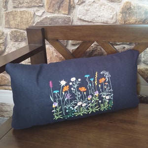 Peut inclure: Un coussin bleu fonc&eacute; avec un motif brod&eacute; de fleurs sauvages color&eacute;es sur fond blanc.