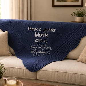 May include: A navy blue quilted throw blanket featuring a scalloped edge and intricate circular stitching patterns. The blanket is embroidered with the white text Derek & Jennifer Morris, the date 07-19-25, and the phrase You will forever be my always.