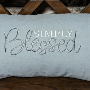May include: A light blue throw pillow with the text "SIMPLY BLESSED" embroidered in white and gray.