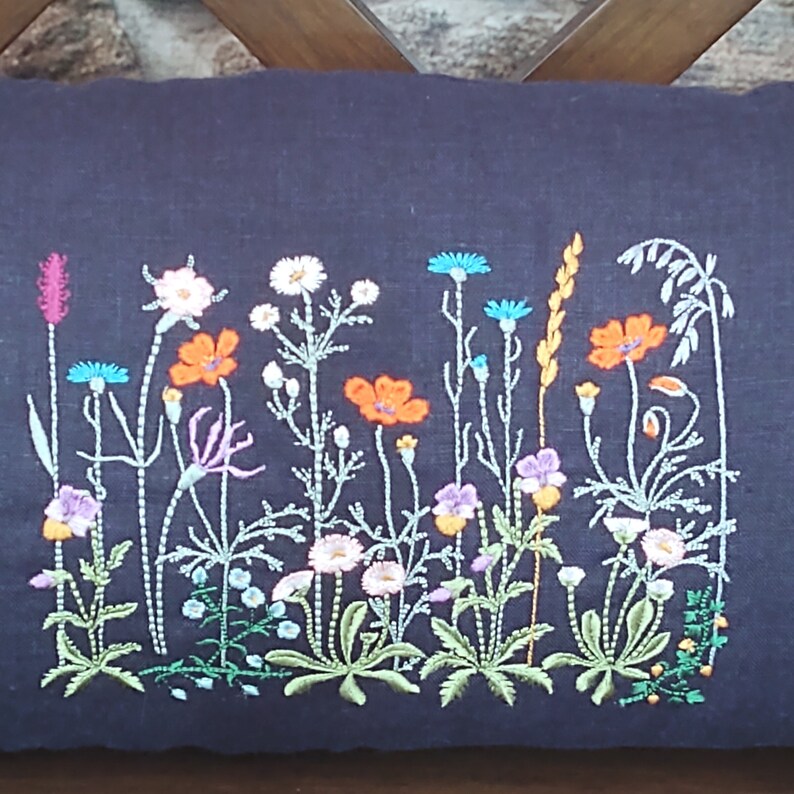 Peut inclure: Un coussin en lin noir avec des fleurs sauvages brod&eacute;es dans des tons d'orange, rose, blanc, bleu et vert.