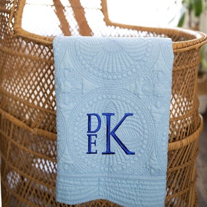 May include: A light blue baby blanket with a white quilted pattern and blue embroidered initials "D.E.K."