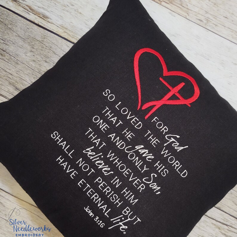 May include: Black throw pillow with white text and a red embroidered heart with a cross. The text reads "For God so loved the world that he gave his one and only Son, that whoever believes in him shall not perish but have eternal life. John 3:16."