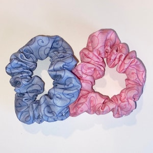 May include: Two fabric scrunchies, one blue with a swirl pattern and one pink with a swirl pattern.
