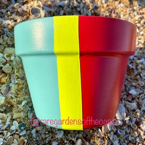 Peut inclure: Un pot en terre cuite peint en trois bandes verticales turquoise, jaune et rouge.
