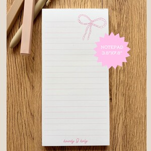 May include: A white notepad with pink lines and a pink rope bow design. The notepad is 3.8 inches by 7.8 inches and has the text "howdy & holy" printed at the bottom.