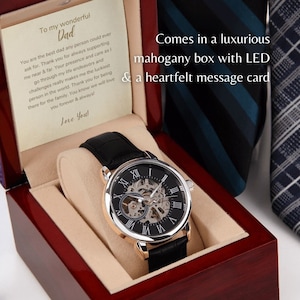 May include: A black leather wristwatch with a silver and gold face and Roman numeral markings. The watch is in a mahogany box with a heartfelt message card. The card reads "To my wonderful Dad".