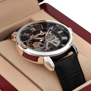 May include: A silver and rose gold watch with a black leather band and a skeletonized dial with Roman numeral hour markers.