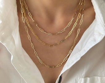 May include: Three gold chain necklaces with a paperclip link design. The necklaces are layered on top of each other.