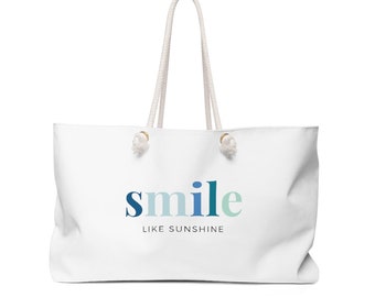 May include: White canvas tote bag with white rope handles. The bag has a blue and green gradient design that says "smile like sunshine" on the front.