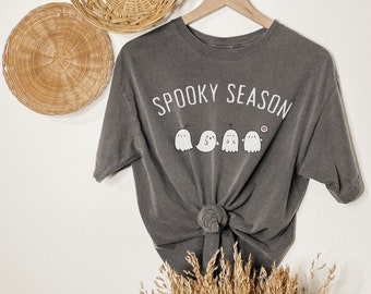 May include: A dark gray t-shirt with the text "Spooky Season" printed in white. Five small white ghosts with black eyes and mouths are lined up below the text.