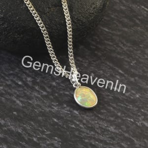 May include: A silver necklace featuring an oval opal pendant. The opal displays yellow, green, and white hues. The chain is a curb link design. The image includes the text "GemsHeavenIn".