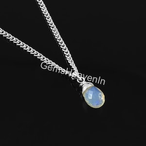 May include: A silver chain necklace featuring a pear-shaped, faceted opal pendant. The opal has a pale blue and yellow hue. The chain is a curb style, and the pendant is wire-wrapped. The background is black.