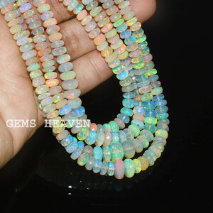 May include: A strand of iridescent opal beads, featuring a mix of white, green, and pink hues. The beads are oval-shaped and have a smooth, polished finish.