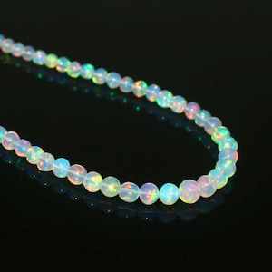 May include: A strand of iridescent opal beads. The round beads are white with flashes of blue, green, and red. The beads are strung together, creating a necklace.