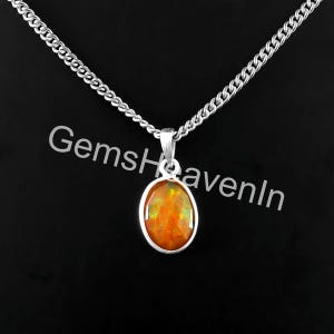 May include: A silver necklace with an oval, orange gemstone pendant. The gemstone has a faceted surface and is set in a silver bezel. The chain is a curb style, and the background is black. The text "GemsHeavenIn" is visible.