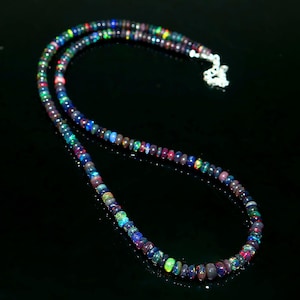 May include: A necklace composed of small, colorful beads. The beads display a range of colors, including blue, green, red, and purple. The necklace has a silver clasp and is displayed against a black background.