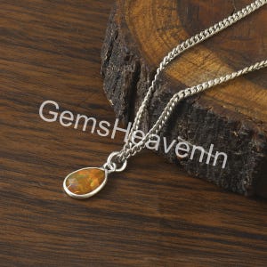 May include: A silver necklace with a teardrop-shaped pendant. The pendant has an orange and yellow gemstone. The chain is a curb style. The text "GemsHeavenIn" is printed on the surface.