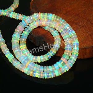 May include: A strand of iridescent opal beads, with a mix of white, green, blue, and pink hues. The beads are round and have a smooth, polished finish. The strand is displayed on a wooden surface.