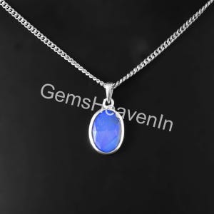 May include: A silver necklace featuring an oval, blue gemstone pendant. The pendant is set in a silver frame and suspended from a fine chain. The image includes the text "GemsHavenIn".