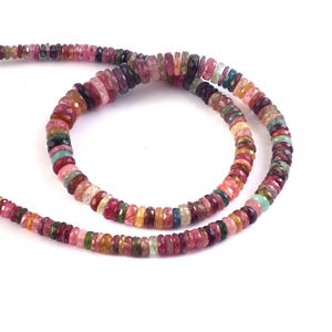 Puede incluir: Un collar de cuentas de turmalina multicolores. Las cuentas son una mezcla de tonos rosas, rojos, verdes, amarillos y azules. Las cuentas son pequeñas, planas y redondas, y están ensartadas para formar un collar o pulsera.