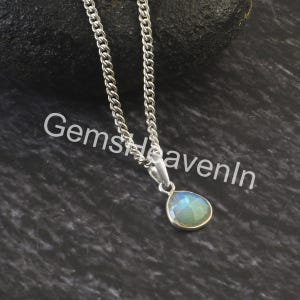 May include: A silver necklace featuring a pear-shaped pendant with a light blue and green iridescent gemstone set in a gold-coloured bezel. The chain is a curb style. The text "GemsHeavenIn" is visible.