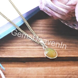 May include: A silver necklace featuring a small, teardrop-shaped pendant with a yellow and green gemstone. The chain is a delicate curb link style. The text "Gems HeavenIn" is visible.