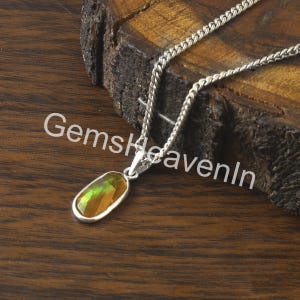 May include: A silver necklace with a pendant featuring a faceted, oval gemstone with green and orange tones. The pendant is set in a silver bezel and hangs from a delicate chain. The text "GemsHeavenIn" is visible.