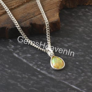 May include: A silver necklace featuring a pear-shaped opal pendant with iridescent colours. The pendant is set in a silver bezel and suspended from a fine chain. The text "GemsHeavenIn" is visible.