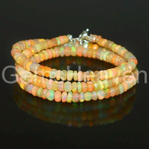May include: A multi-strand necklace composed of small, rounded opal beads. The beads display a range of colors, including orange, yellow, and hints of green. The necklace is secured with a silver clasp, and the overall design is elegant.