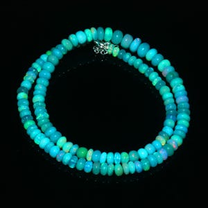Op de afbeelding: Een ketting bestaande uit twee strengen turquoise opaal kralen. De kralen, variërend in grootte, zijn geregen met een zilveren sluiting. De opaal kralen hebben een glanzende afwerking, die licht reflecteert en een glinsterend effect creëert.