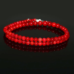 May include: A double-strand necklace featuring vibrant red beads. The beads are small and round, strung together with a silver clasp. The necklace is displayed against a black background, creating a striking contrast.