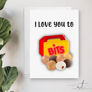 May include: A white greeting card with the text "I Love you to" above a graphic of a yellow and red box of "Bits" and various chocolate-covered treats. The card is inside a white envelope.