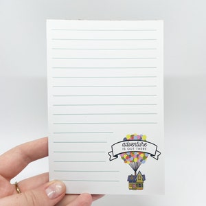 May include: A lined notepad with a colorful illustration of a house with balloons and the text "adventure is out there".