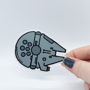 Puede incluir: Una pegatina gris y negra del  Millennium Falcon, la nave espacial de Star Wars.