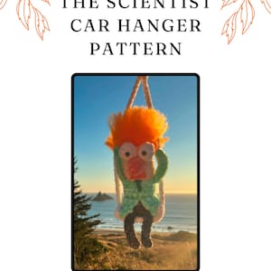 May include: A crochet car hanger pattern for a scientist character named "Beaki" by Funniface05. The character is orange, green, and black and is hanging from a white string.