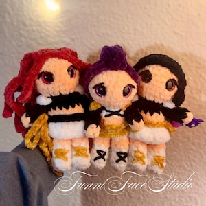 May include: Three handmade crochet dolls with plush bodies, each with a unique hairstyle and outfit. The dolls have large eyes and are in shades of red, purple, and black. The text "Funni Face Studio" is visible at the bottom.