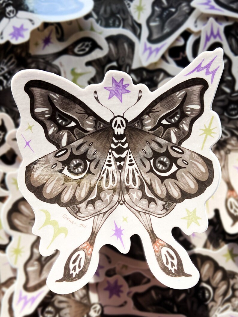 May include: A black and white illustration of a moth with a skull on its body. The moth has large, detailed eyes and is surrounded by small stars and lightning bolts. The artist's signature, "@karli_jay", is in the lower left corner.