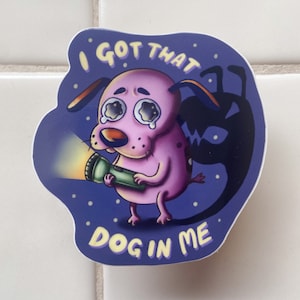May include: A sticker featuring a cartoon dog with large, tearful eyes holding a flashlight. The dog is pink with a purple background and the text "I GOT THAT DOG IN ME". A black shadow figure is behind the dog.