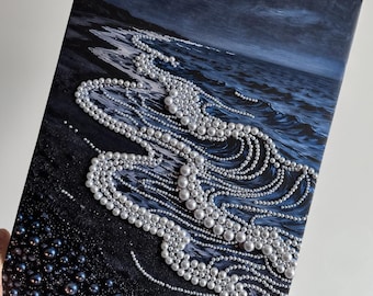 May include: Canvas art print depicting a dark ocean scene with waves and a beach. The waves are embellished with strings of white pearls, creating a unique texture. The artwork is held at an angle.