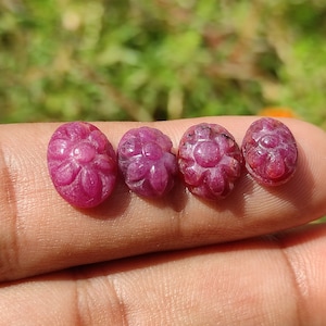 Op de afbeelding: Vier roze, ovale edelstenen met gegraveerde bloemmotieven. De edelstenen zijn in een rij op een vinger gerangschikt.