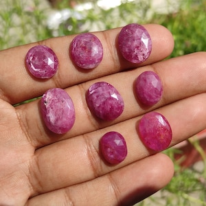 May include: A collection of eight oval-shaped, pink gemstones with a faceted cut. The gemstones are displayed on a hand.