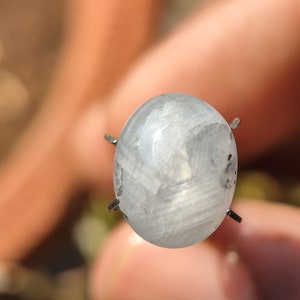 May include: A clear, round gemstone with a silvery sheen, held in place by four metal prongs.
