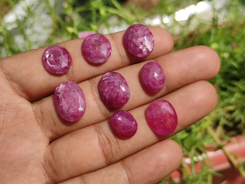 Pu&ograve; includere: Una collezione di otto pietre preziose rosa sfaccettate di forma ovale. Le pietre preziose sono esposte su una mano.