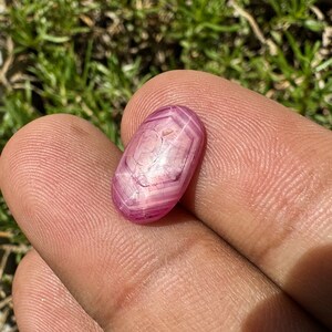 May include: A pink star ruby gemstone with a hexagonal facet pattern. The gemstone is oval shaped and has a smooth, polished surface.