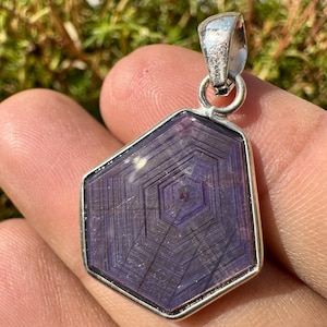 May include: A silver pendant featuring a hexagonal purple gemstone with a starburst pattern. The gemstone is set in a silver bezel.