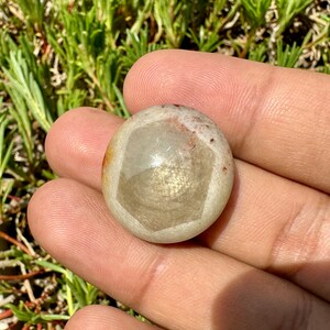 May include: A round, white and grey gemstone with a geometric pattern. The stone has a smooth, polished surface.
