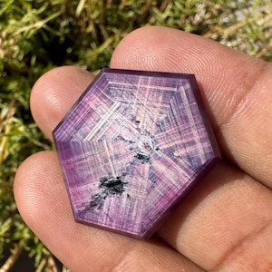 May include: A hexagonal, faceted, purple gemstone with a star-like pattern and black inclusions.
