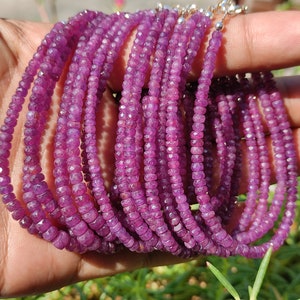 Op de afbeelding: Een streng roze robijn kralen, gefacetteerd en geregen op een zilveren ketting. De kralen zijn klein en uniform in grootte, wat een delicate en elegante uitstraling creëert.