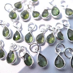 Op de afbeelding: Een verzameling zilveren hangers in druppelvorm met groene edelsteenaccenten. De hangers hebben een lus aan de bovenkant om aan sieraden te bevestigen.